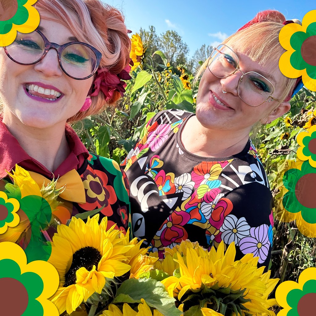 Two smiling women stand in a sunflower field, dressed in colorful and sustainable fashion outfits.