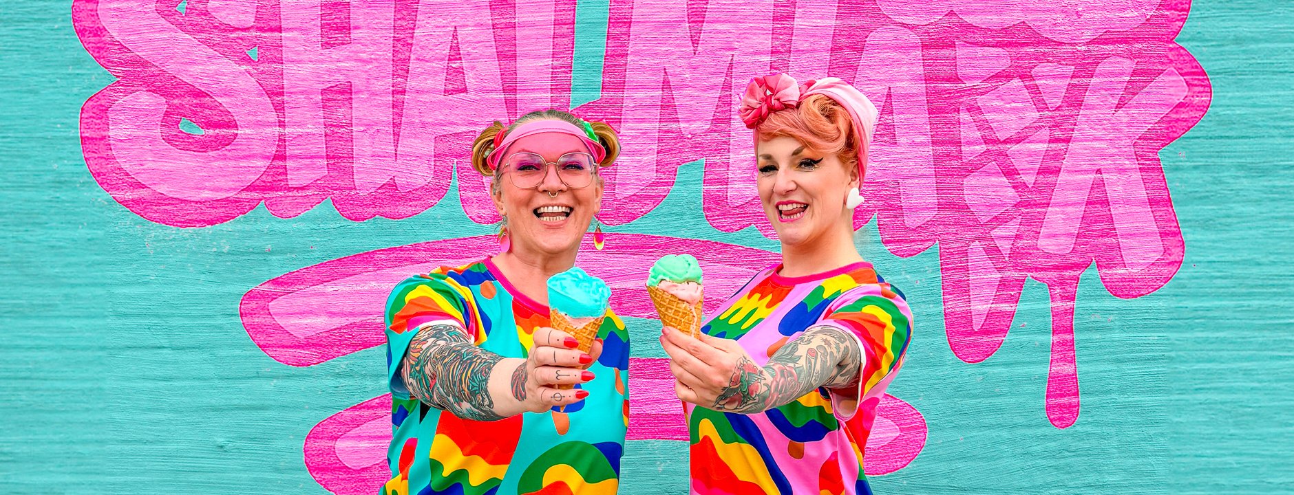 Two cheerful women holding ice cream cones in bold MANIC ICE t-shirt dresses by SHALMIAK.
